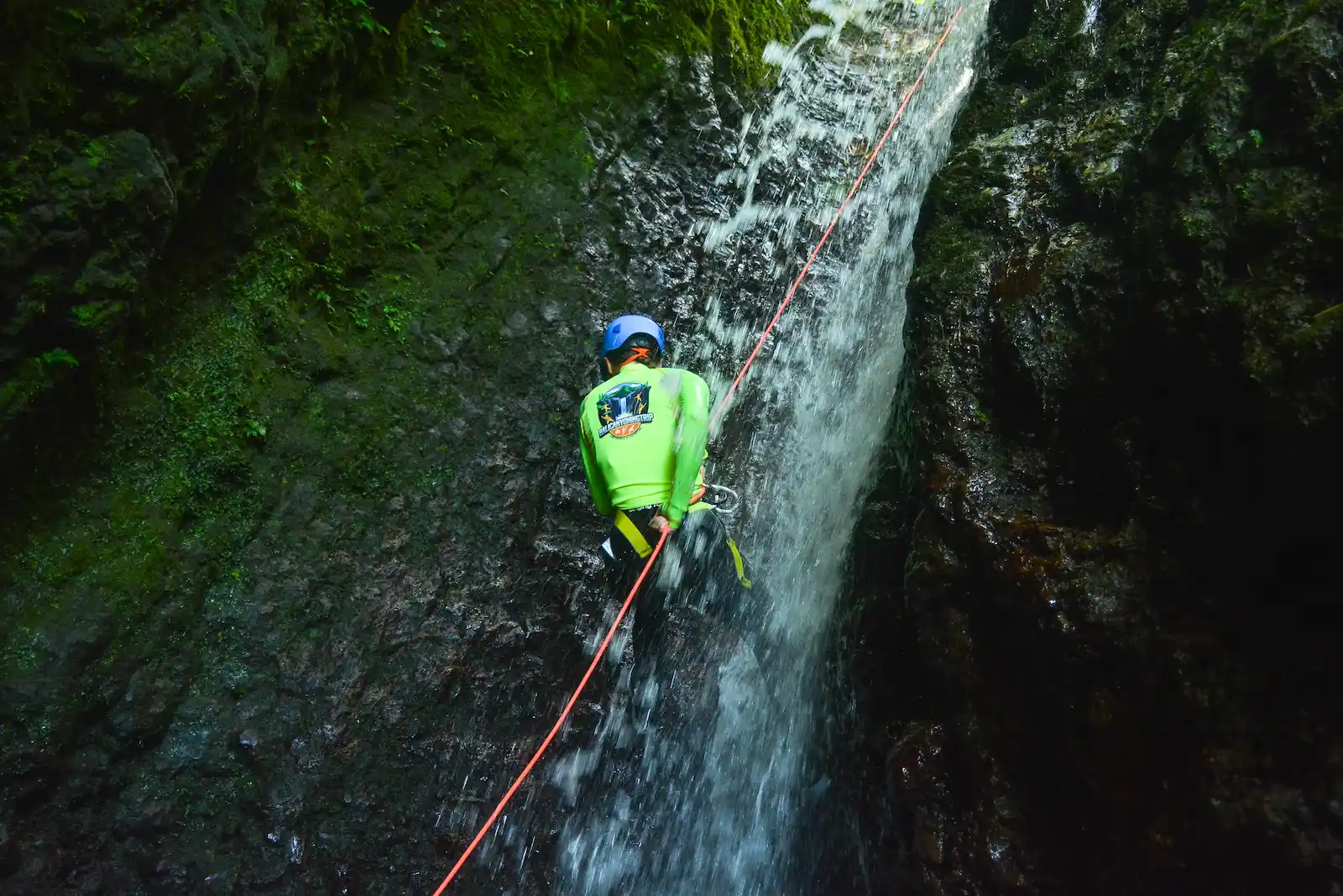 Three canyoners descending on blue and orange ropes with guide-managed rope systems in a mossy North Bali canyon
