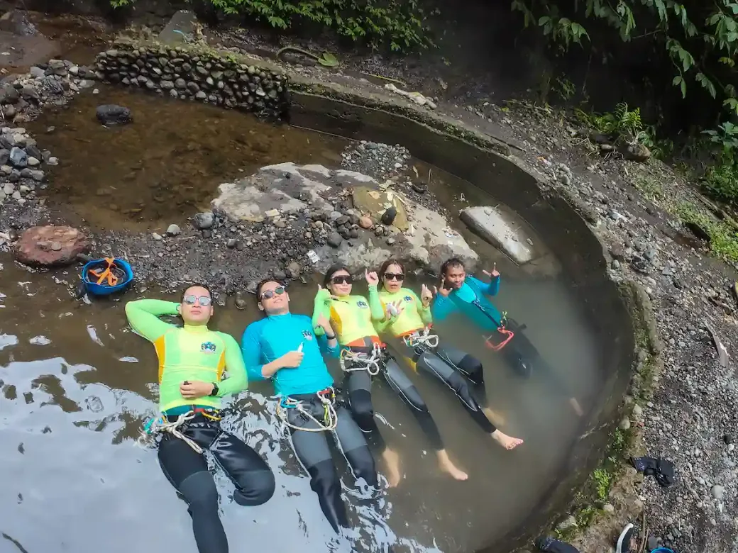 A group of canyoners in wetsuits and harnesses lying back in the hot spring pool in Gitgit Canyon