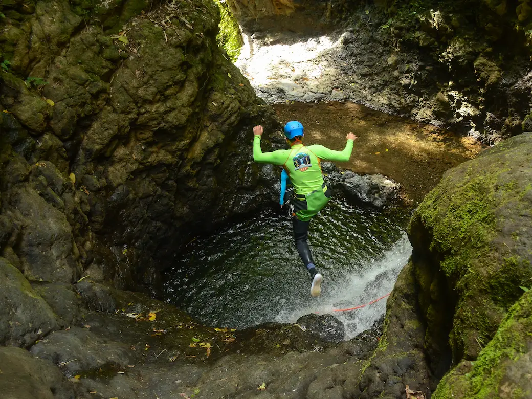 A canyoner in a green top leaping into a clear natural pool during an optional jump in a Bali canyon