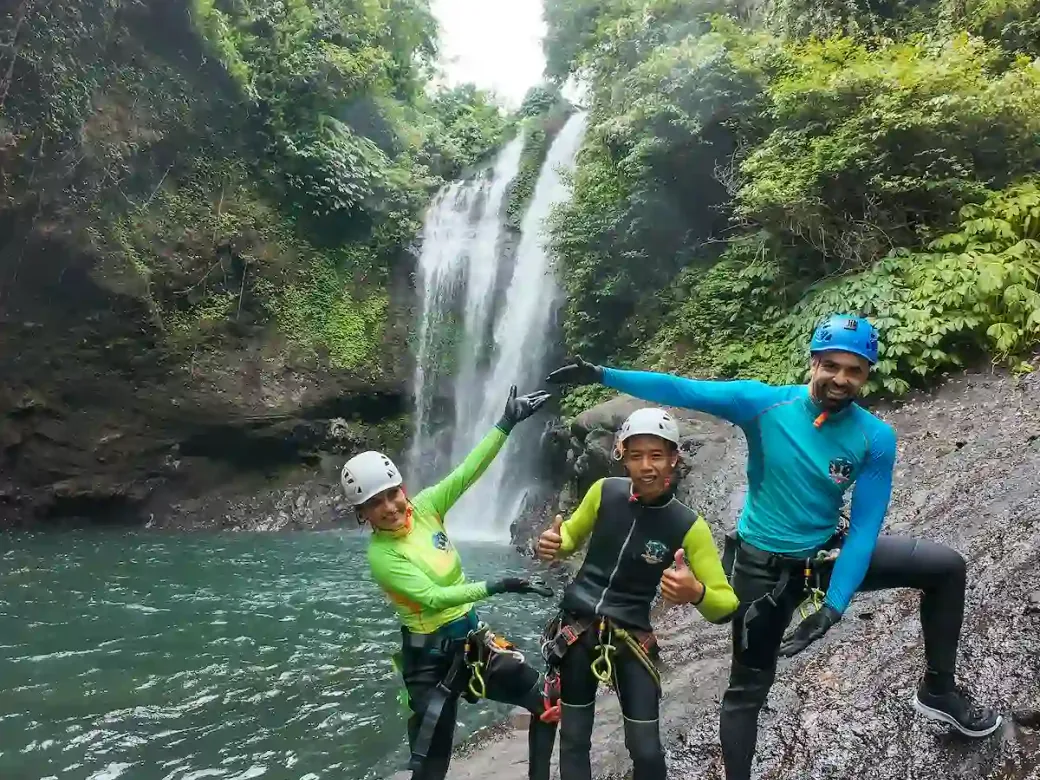 Three canyoners in helmets and harnesses posing in front of Aling-Aling waterfall