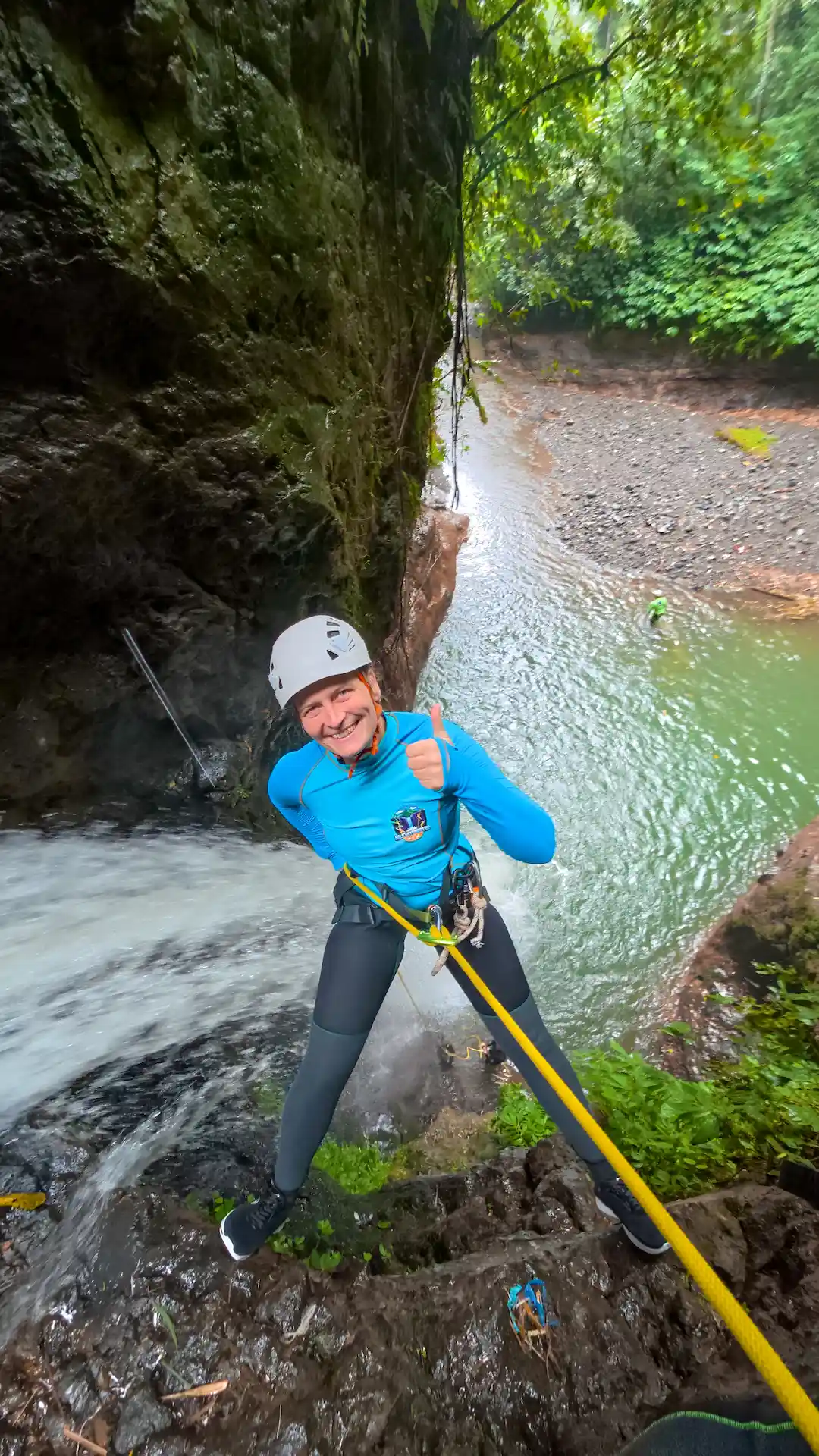 Guest rappelling down the face of a jungle waterfall