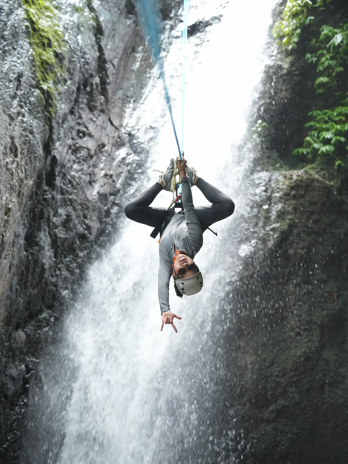Backflip-style pose hanging from the rope in front of the waterfall