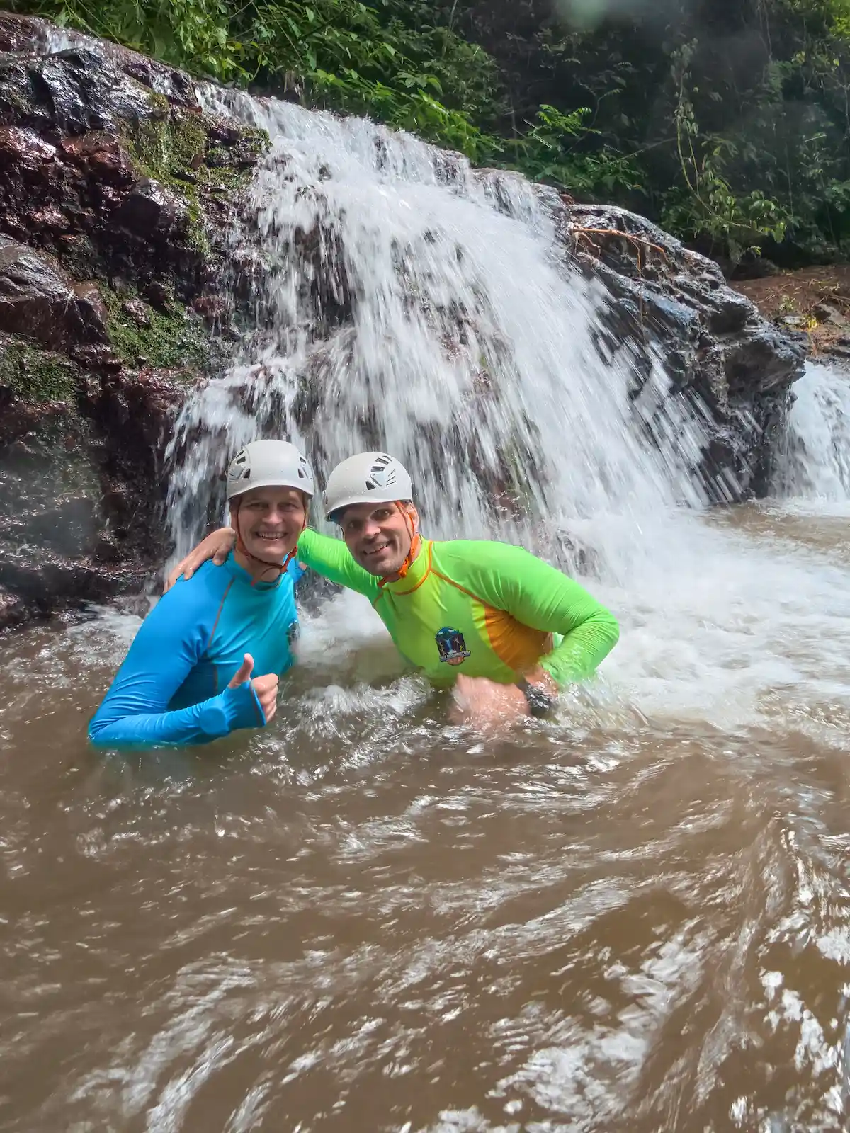 Two guests smiling in the pool beneath a waterfall on Splash Canyon