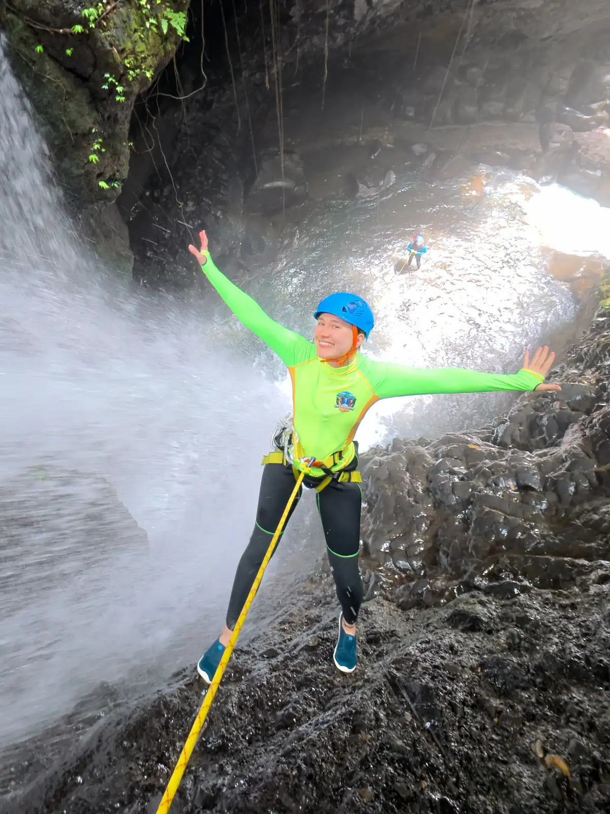 A canyoner rappelling on rope beside a waterfall under guide supervision in North Bali